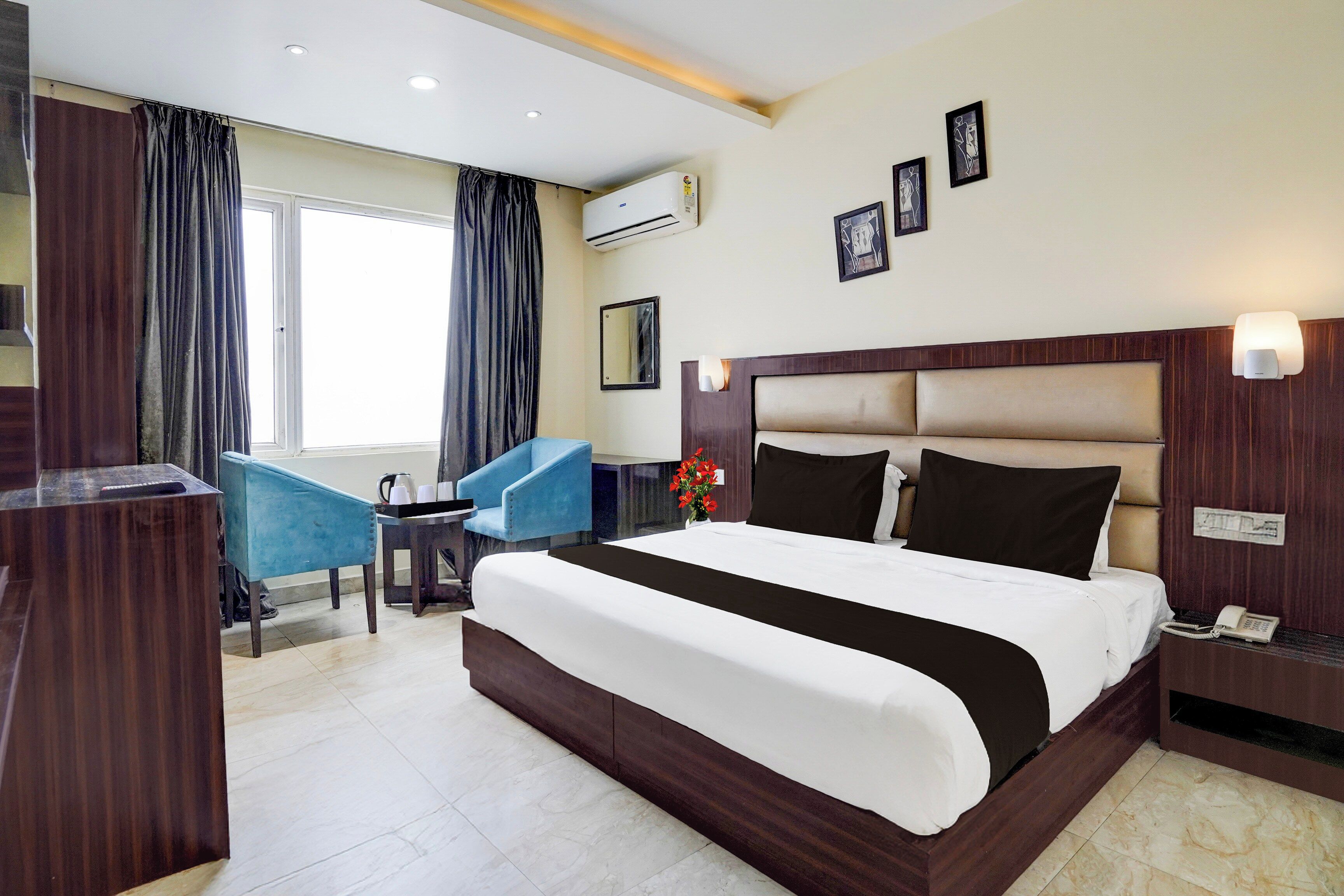 A hotel room with a large bed, a desk, a chair, a desk lamp, and a wall-mounted phone.