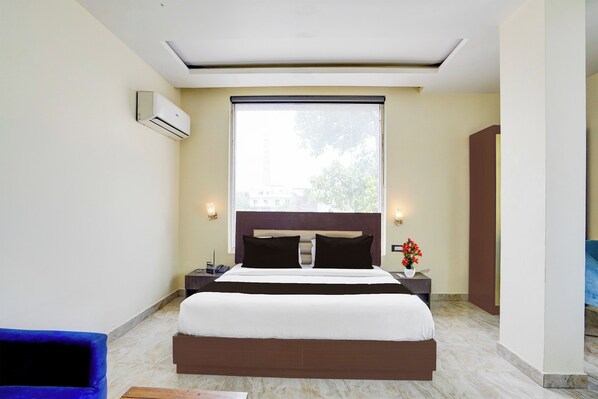 A hotel room with a large bed, a window, a nightstand, and a wall-mounted air conditioner. - Collection O Railway Station Dehradun (Dehradun)