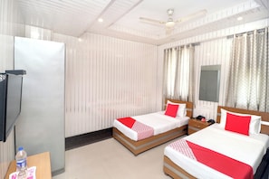 A hotel room with two beds, a television, a desk with a bottle and glasses, and a ceiling fan. - Hotel O Le Bon Ton (Ludhiana)