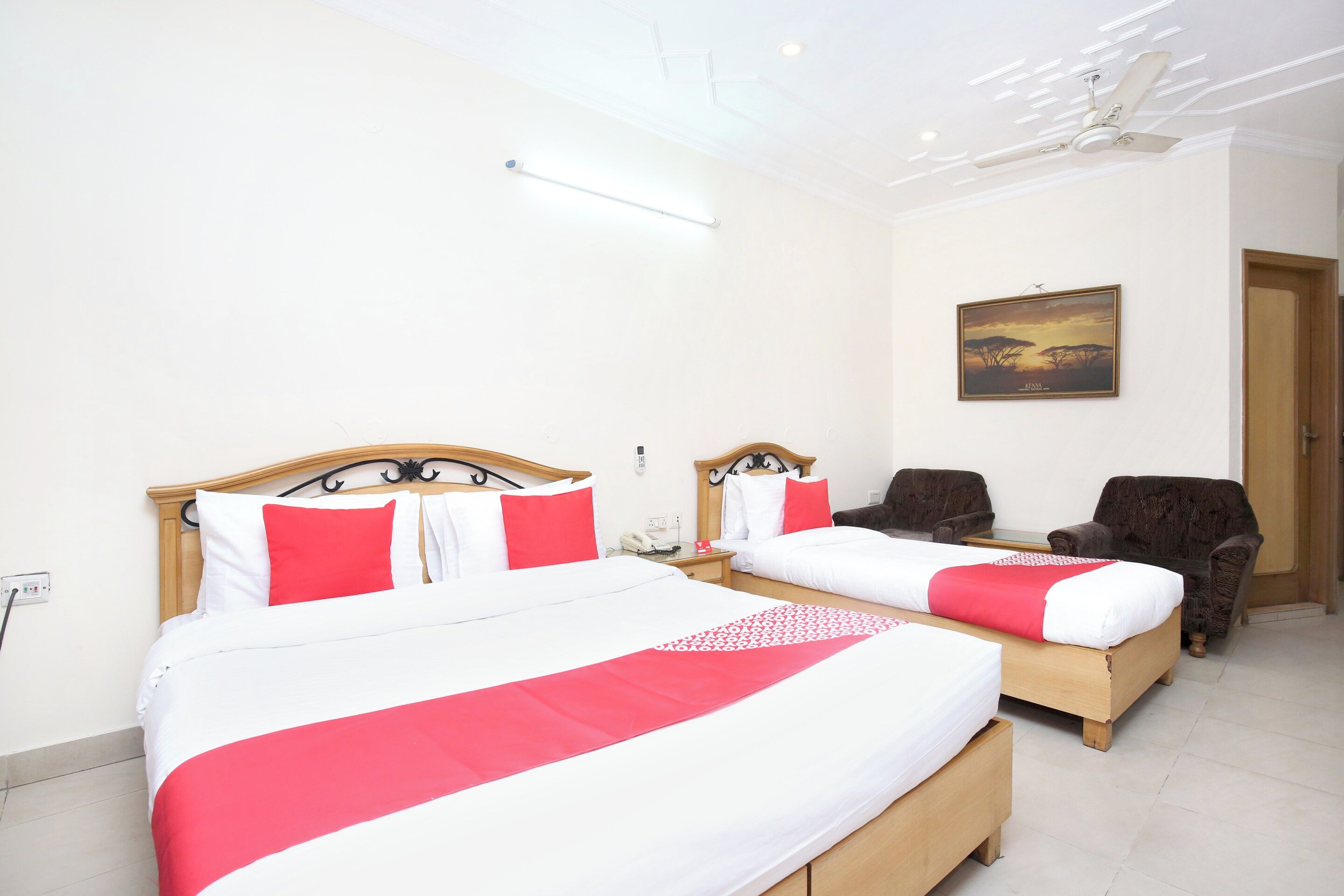 A hotel room with two beds, a ceiling fan, a painting, and a door.