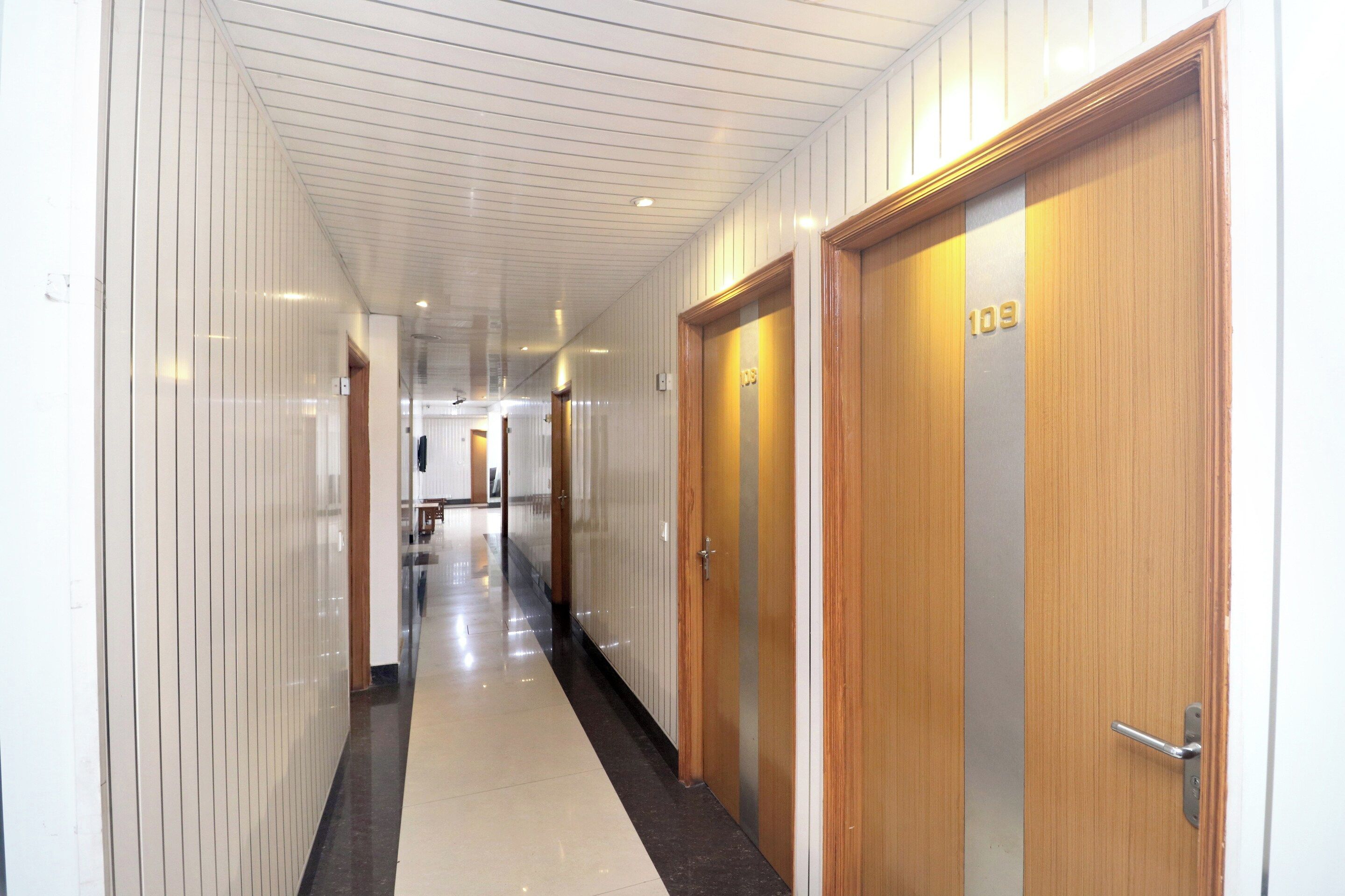 A hotel corridor with wooden doors, a tiled floor, and a ceiling with recessed lighting.