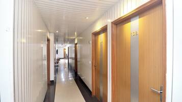 A hotel corridor with wooden doors, a tiled floor, and a ceiling with recessed lighting.
