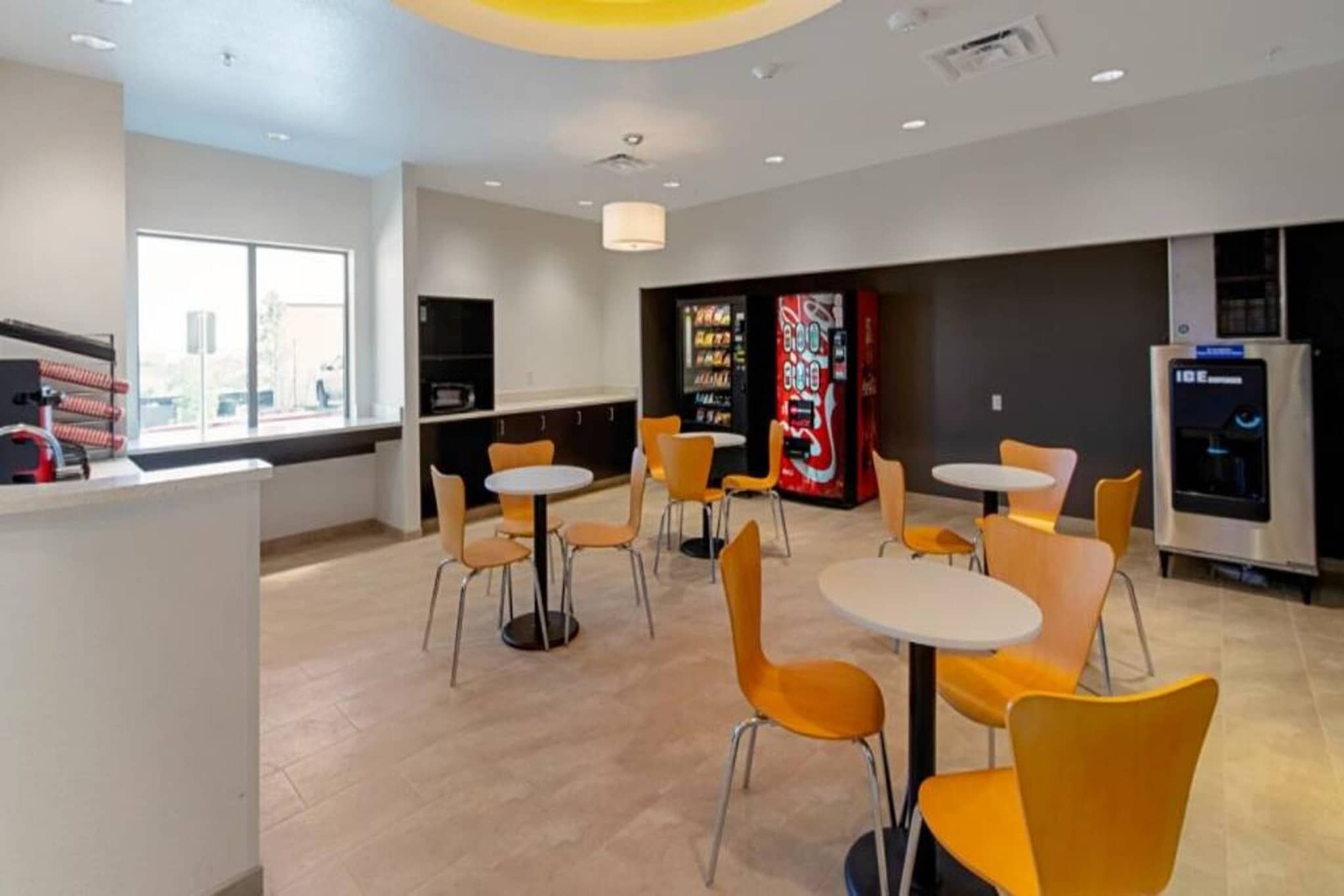 A modern interior with round tables and chairs, vending machines, and a water dispenser.