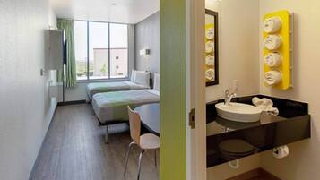 A hotel room with two beds, a chair, a window, and a bathroom with a sink and towel rack.