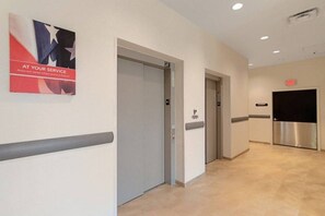 Un couloir avec une affiche sur le mur, une porte et un ascenseur.