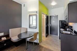 Un espace de vie compact comprenant un coin cuisine, un coin repas avec une table et des chaises, et un petit coin salon avec un banc.