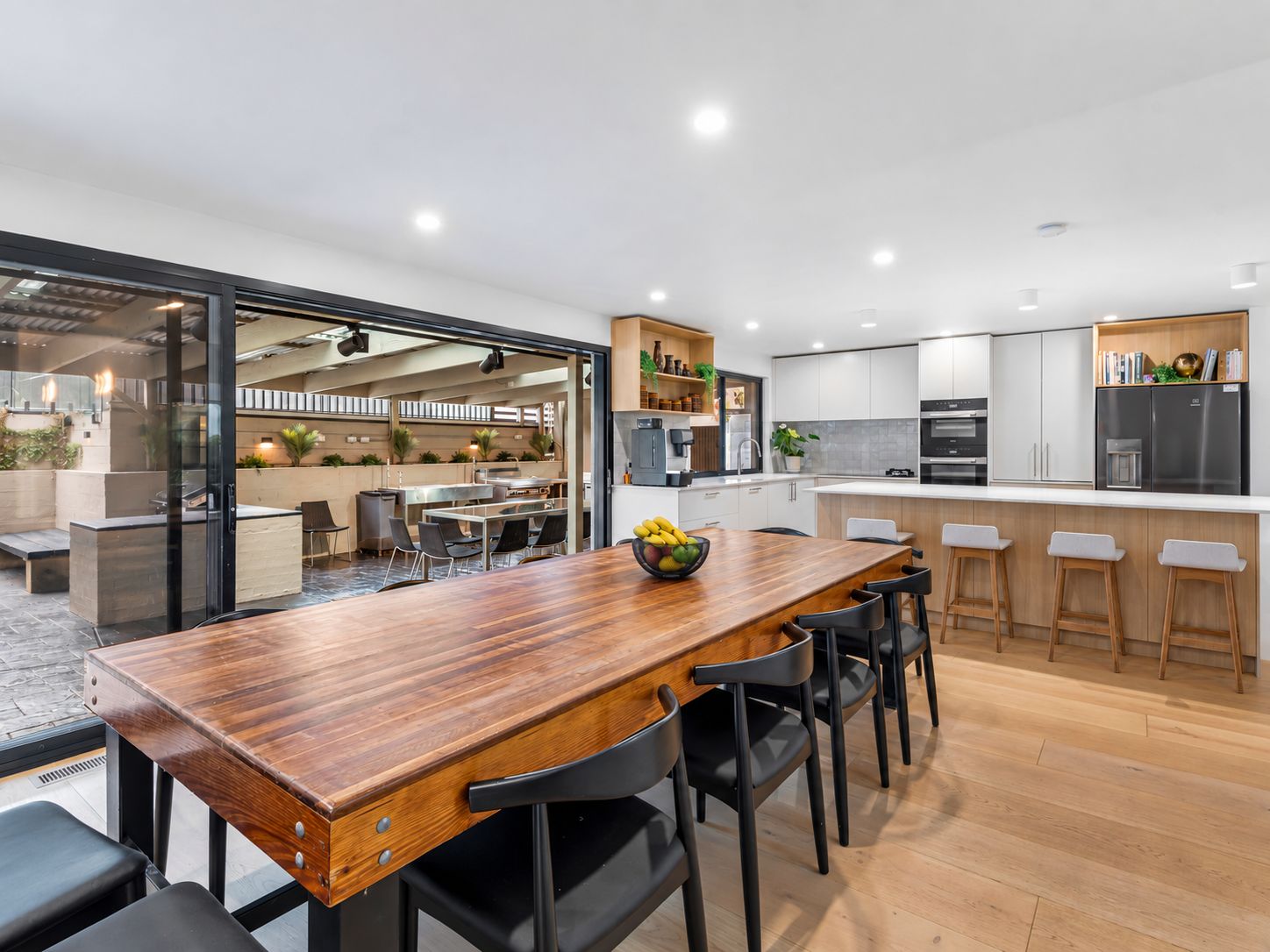 A modern kitchen with white cabinets, a wooden dining table, and a view into the dining area.