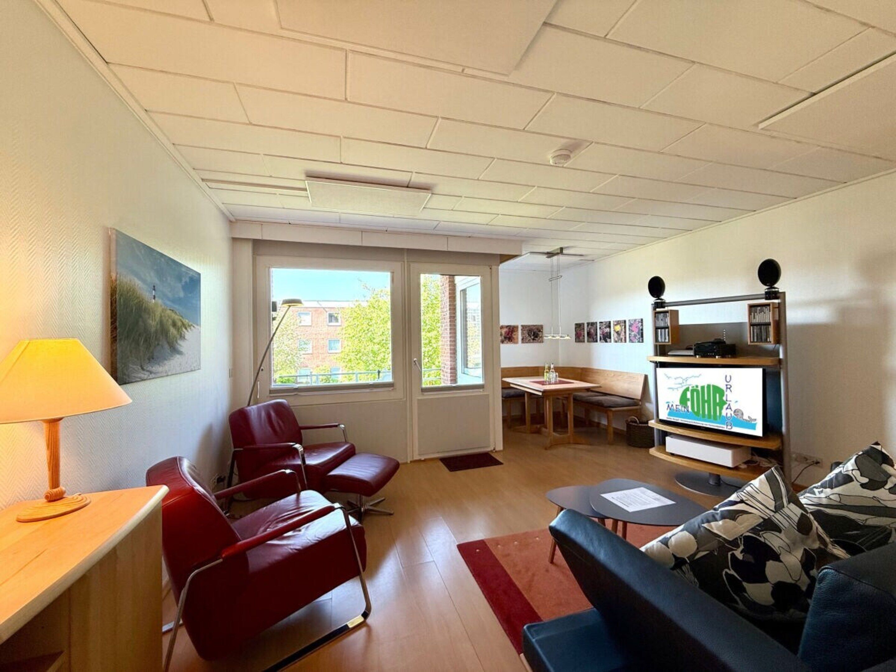 A modern living room with a red sofa, a blue couch, a wooden table, and a bookshelf.