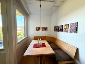 Ein Zimmer mit einer Holzbank, einem Tisch mit roter Tischdecke und Wandbildern.