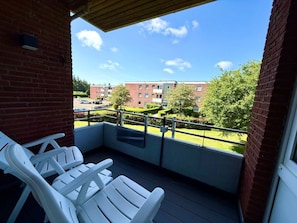 Ein Balkon mit weißen Stühlen, einem Metallgeländer und Blick auf ein Ziegelgebäude mit einer grünen Rasenfläche.