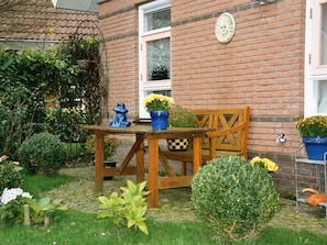 Ein Backsteinhaus mit Holztisch und Stuhl, umgeben von verschiedenen Pflanzen und Blumen.