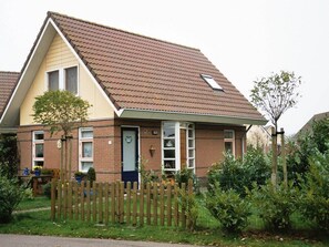 Ein zweistöckiges Haus mit geneigtem Dach, einer Veranda und einem Holzzaun.