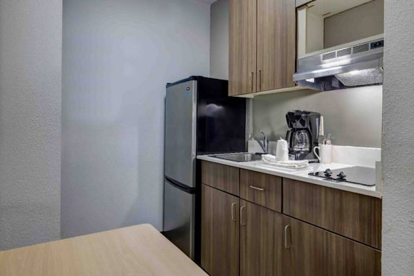 A compact kitchen with a refrigerator, a coffee maker, and wooden cabinets. - 2 Full Beds | Smoking (Arlington)