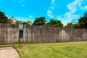 A fenced yard with a green sign, a street lamp, and trees in the background. - 1 Queen Bed | Non-Smoking (Arlington)