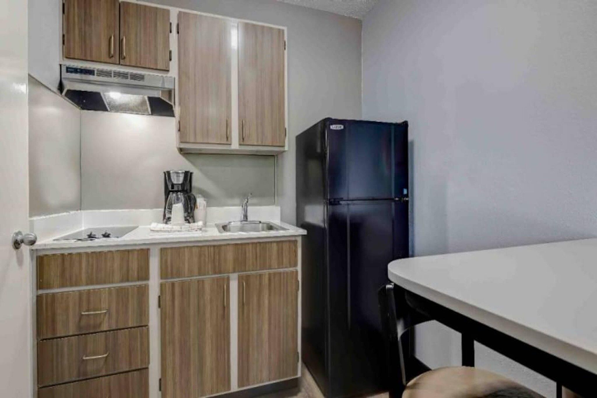 A compact kitchen with wooden cabinets, a black refrigerator, a coffee maker, and a sink.