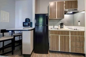A compact kitchen with a refrigerator, a coffee maker, and wooden cabinets. - 1 Queen Bed|ADA/RI Shower| NS (Arlington)