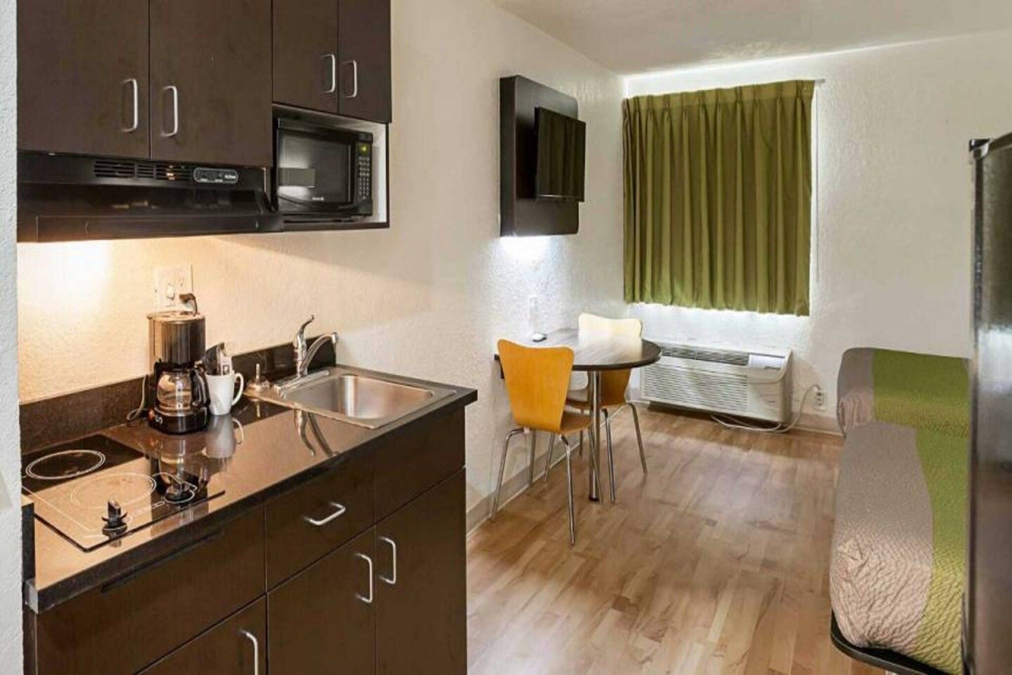 A compact kitchenette with a microwave, coffee maker, and sink. There is a small dining area with a table and chairs.