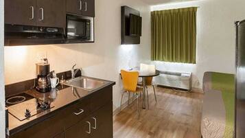 A compact kitchenette with a microwave, coffee maker, and sink. There is a small dining area with a table and chairs.