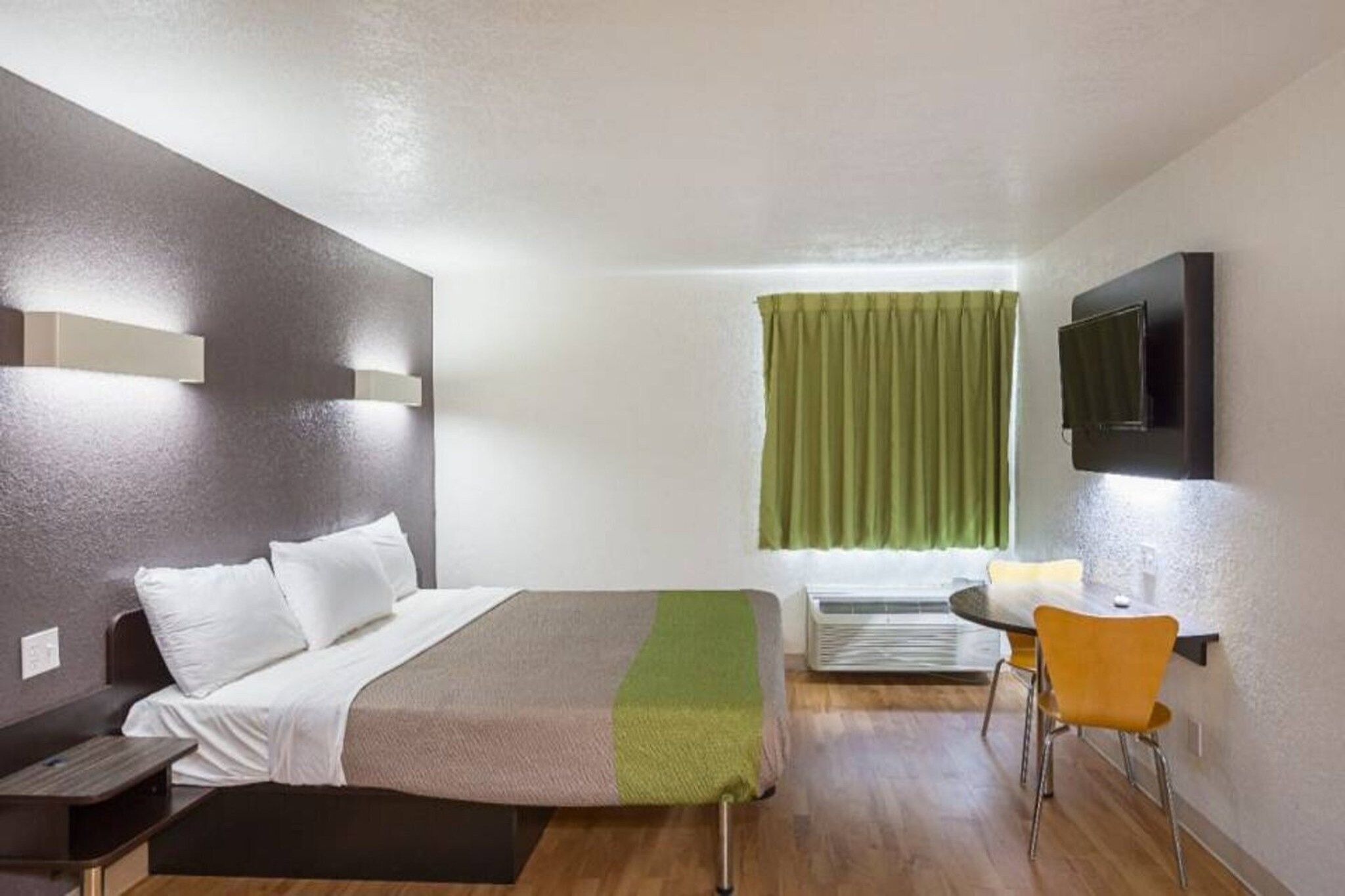 A hotel room with a bed, bedside table, chair, and a television on the wall.