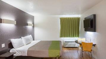 A hotel room with a bed, bedside table, chair, and a television on the wall.