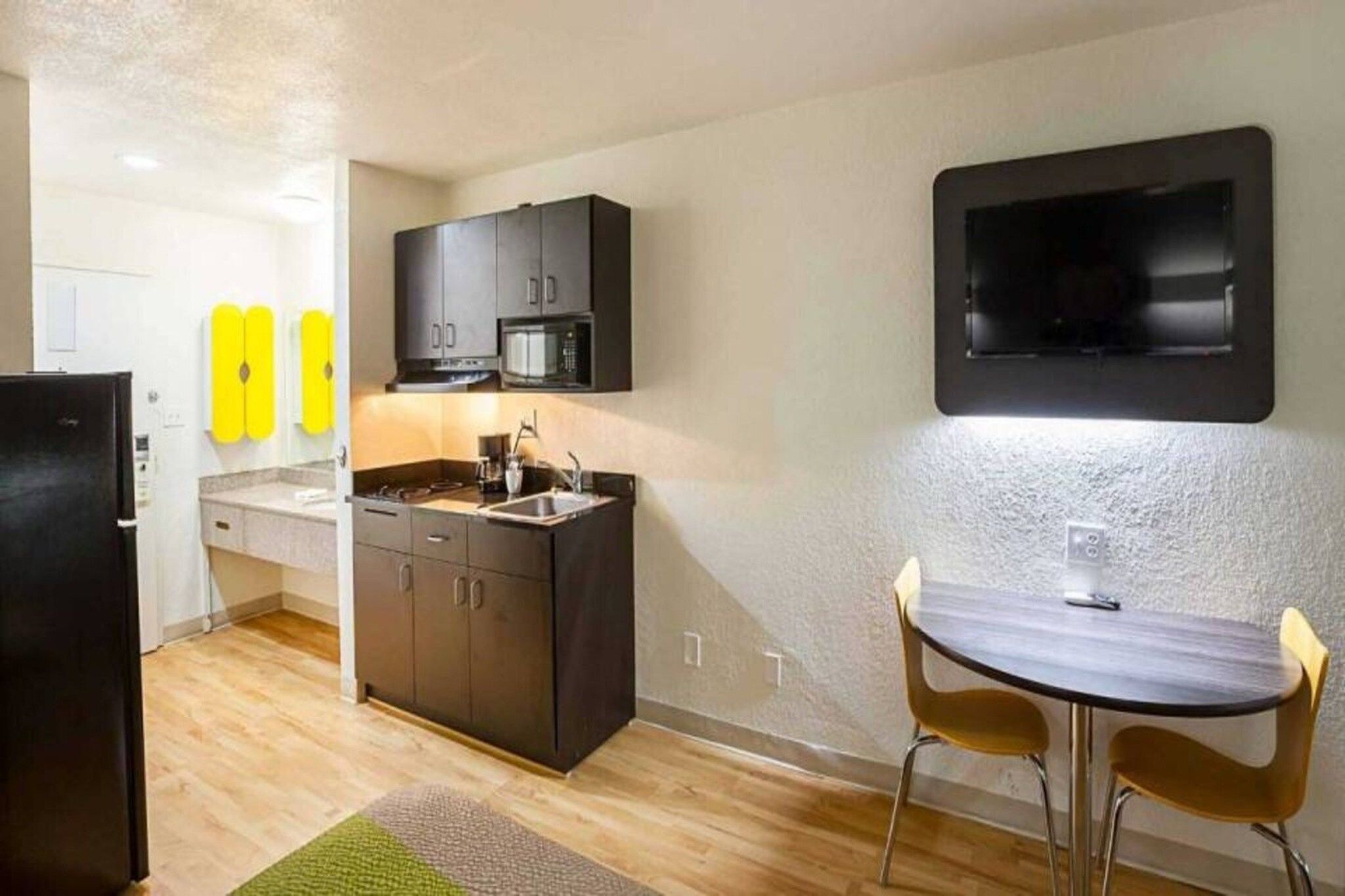 A compact kitchen with dark cabinets, a microwave, and a sink. There's a small dining area with a table and two chairs.