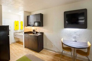 Een compacte keuken met donkere kastjes, een magnetron en een spoelbak. Er is een klein eethoekje met een tafel en twee stoelen.