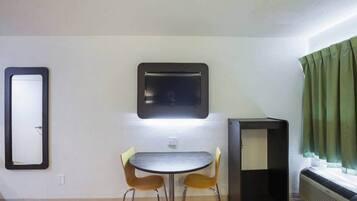 A small room with a round table and two chairs, a wall-mounted TV, a heater, and a window with curtains.