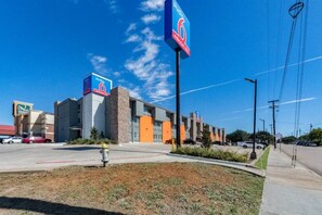 A commercial building with a prominent '6' sign, a parking lot, and a grassy area with a fire hydrant. - 1 King Bed|Smoking| Kitchen (Plano)