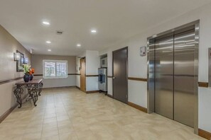 A hotel corridor with a reception desk, a water dispenser, and a large elevator. - 1 King Bed | Non-Smoking, Kitchen (Plano)