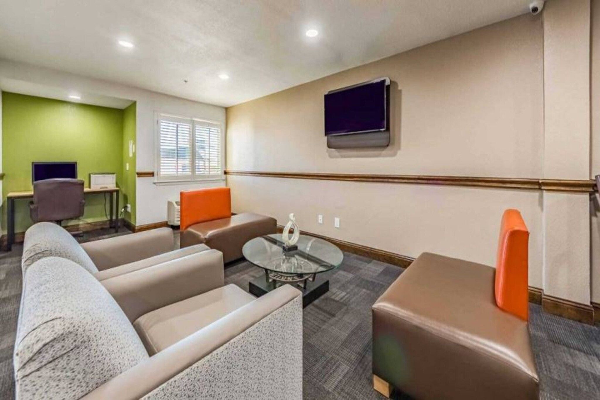 A hotel room with a sofa set, a glass coffee table, and a flat-screen TV mounted on the wall.