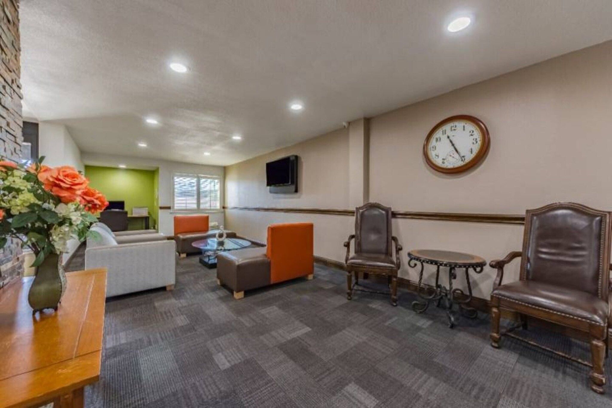 A hotel lobby with seating areas, a clock on the wall, and a television mounted above a table.