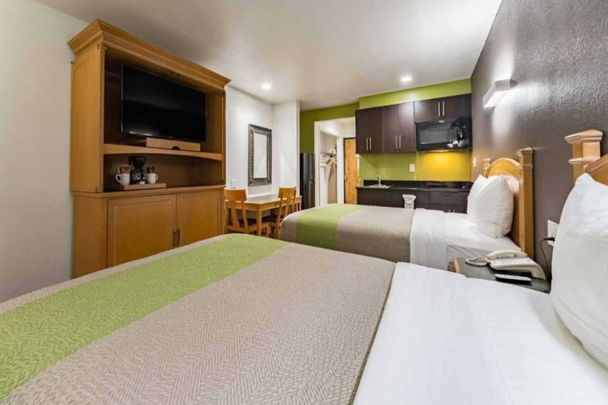 A hotel room with a bed, a TV, a desk, and a kitchenette.