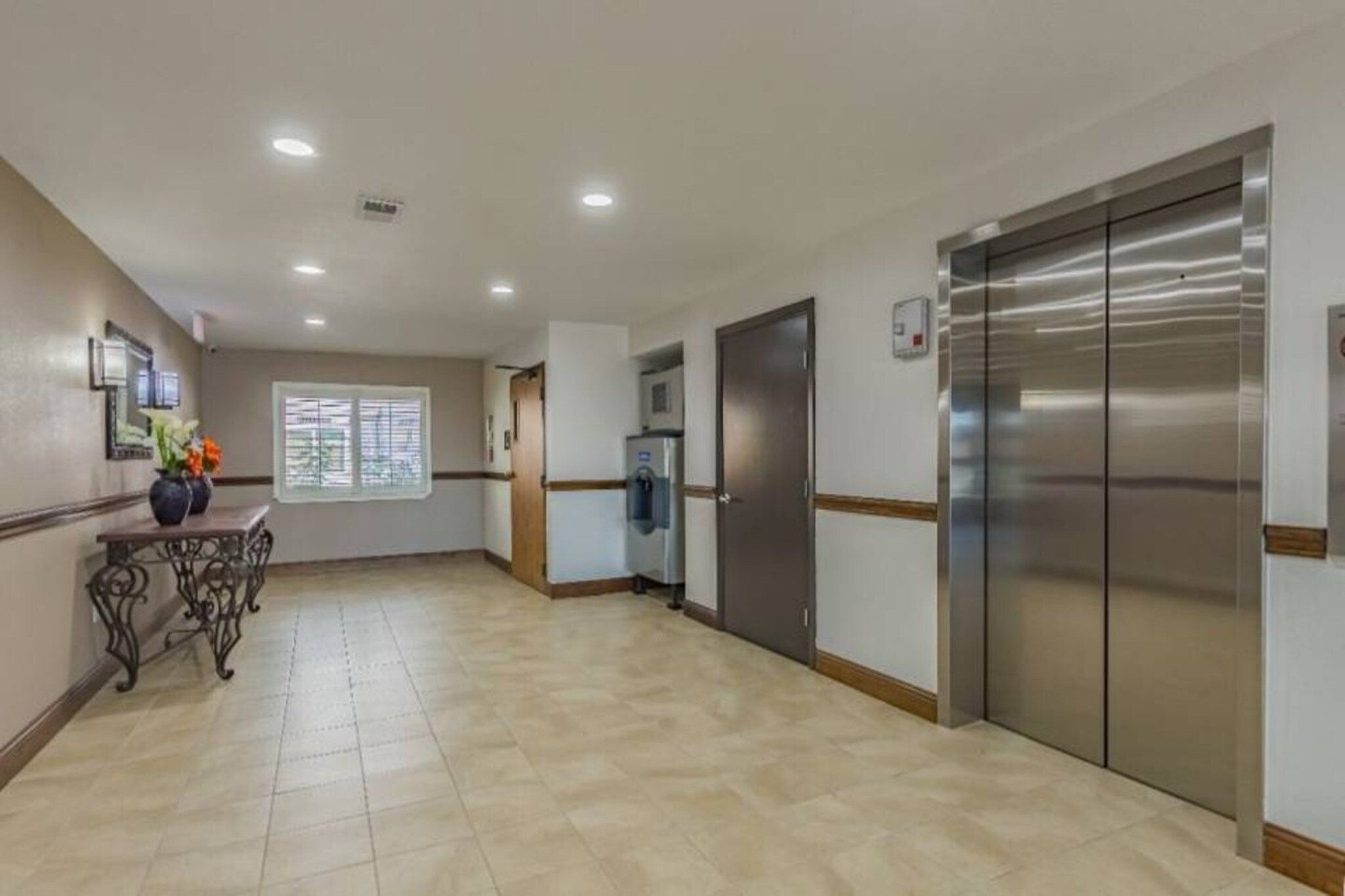 A hotel corridor with a reception desk, a water dispenser, and a large elevator.