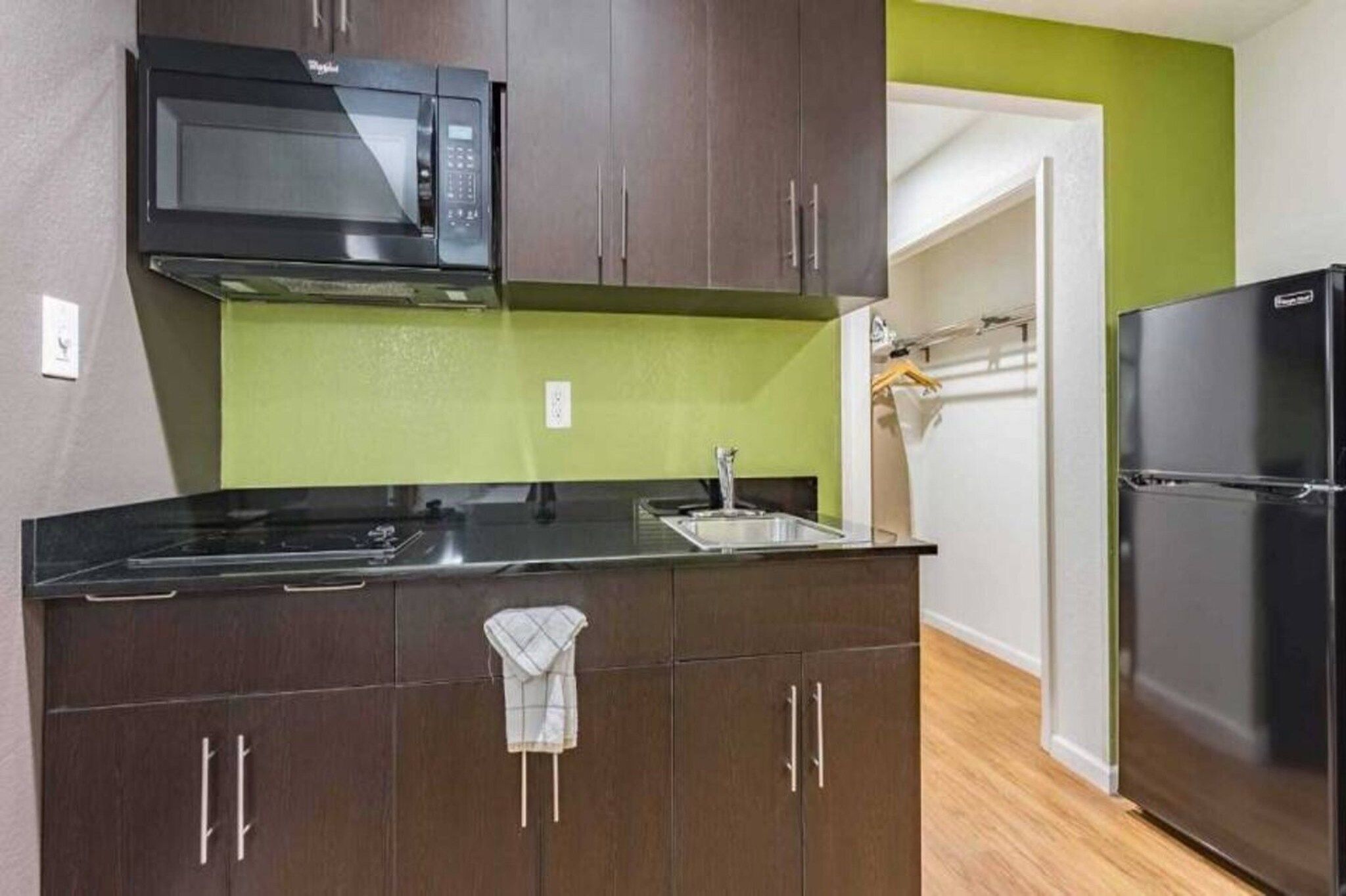A kitchen with dark cabinets, a black microwave, a sink, and a black refrigerator.
