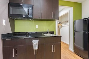 A kitchen with dark cabinets, a black microwave, a sink, and a black refrigerator. - 2 Full Beds|Smoking| Kitchen (Plano)