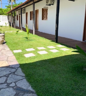 Une cour avec un chemin pavé, un bâtiment blanc doté de volets en bois et une pelouse bien entretenue.