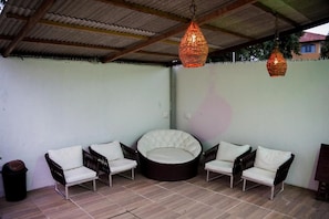 Un espace extérieur abrité, aménagé avec des chaises en osier et un banc circulaire rembourré.