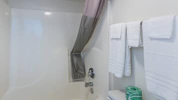 Un baño con bañera, cortina de ducha, inodoro y una pila de toallas blancas.