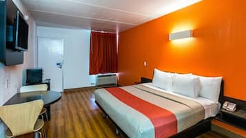 Habitación de hotel con cama, escritorio, silla, televisor y cortina roja.