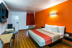 Habitación de hotel con cama, escritorio, silla, televisor y cortina roja.