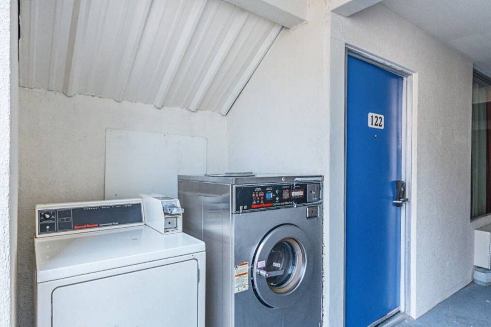 A laundry area with a white dryer, a front-loading washing machine, and a blue door marked with the number 122.