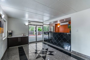 Un vestíbulo de hotel con puerta de cristal, una máquina de café y suelo de baldosas.