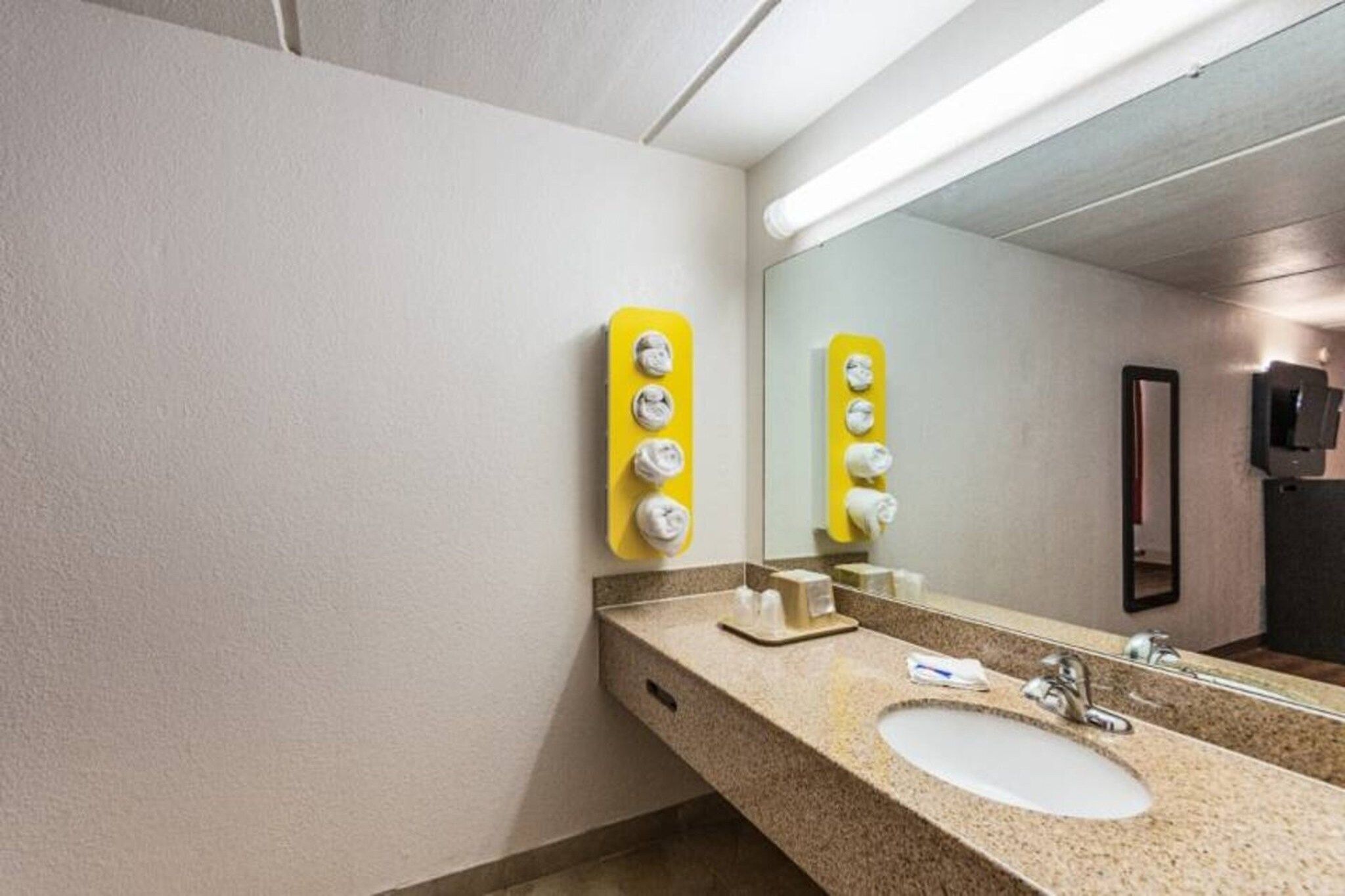 Une salle de bain d’hôtel avec un lavabo, un miroir et des distributeurs de savon jaunes.