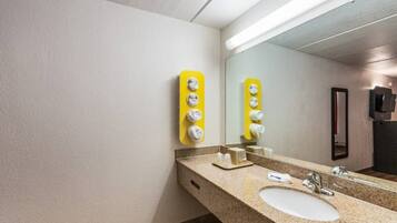 Une salle de bain d’hôtel avec un lavabo, un miroir et des distributeurs de savon jaunes.