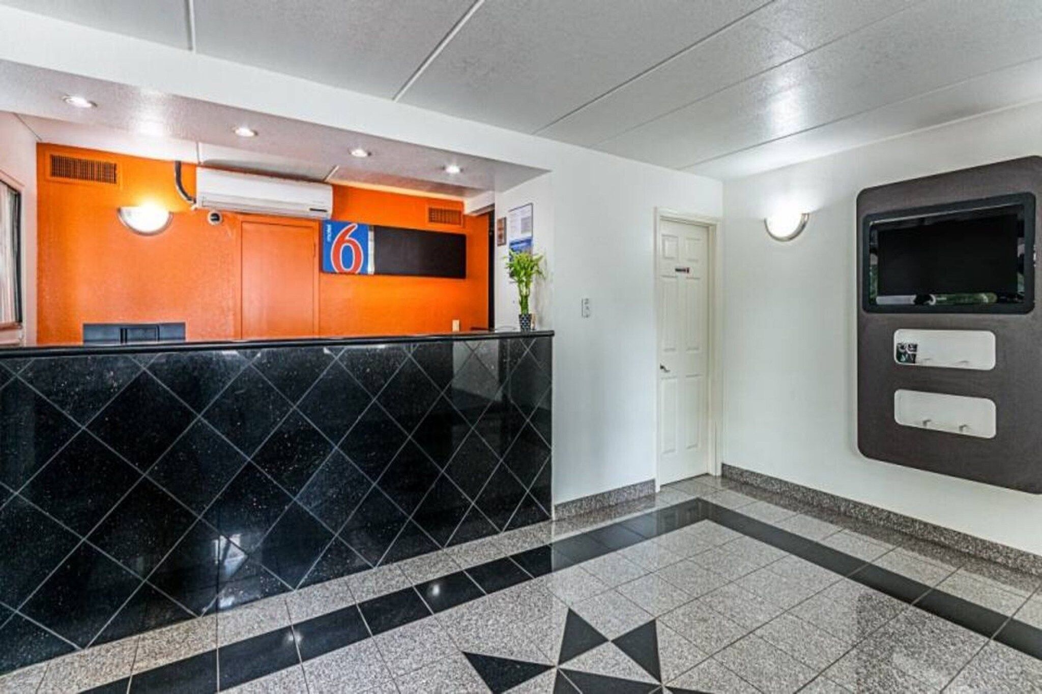 Un área de recepción con mostrador de mármol negro, un letrero con el número 6, una puerta blanca y un quiosco de información adosado a la pared.