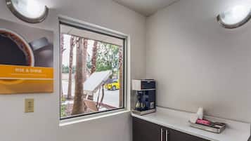 A small kitchenette with a window, a coffee machine, and a sign that reads 'RISE & SHINE'.
