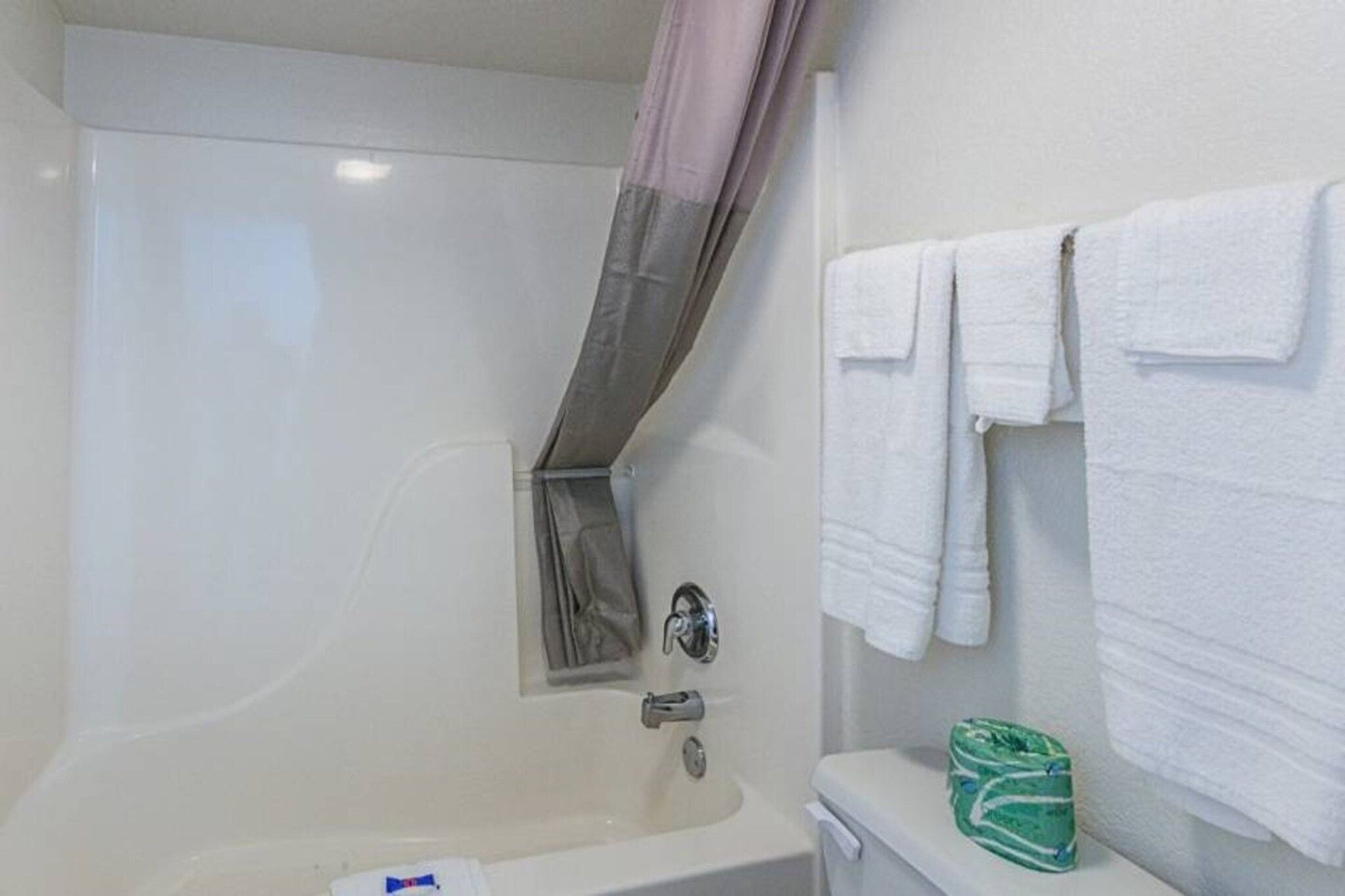 Une salle de bain avec une baignoire, un rideau de douche, des toilettes et une pile de serviettes blanches.