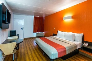 Habitación de hotel con cama, escritorio, silla, televisor y cortina roja.