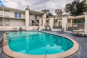 Une piscine entourée d’une terrasse, de chaises longues et d’un bâtiment doté de balcons.