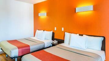 A hotel room with two beds, each with a striped bedspread and white pillows. There are two wall-mounted light fixtures on the orange wall.